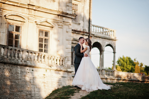 Fabulous wedding couple posing in front of an old medieval castle in the countryside on a sunny day.