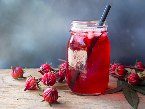 Iced roselle tea glass  with fresh roselle fruit  on wooden table  for healthy herbal drink concept.