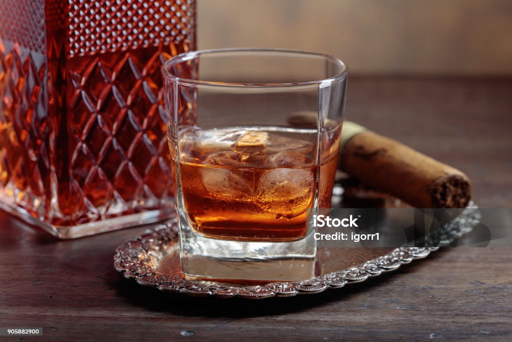 Glass of  whiskey and cigar on old wooden table. Glass of scotch whiskey with natural ice and cigar on old wooden table. Alcohol - Drink Stock Photo