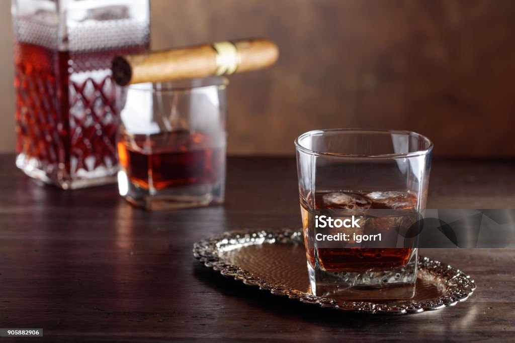 Glass of  whiskey and cigar on old wooden table. Glass of scotch whiskey with natural ice and cigar on old wooden table. Alcohol - Drink Stock Photo