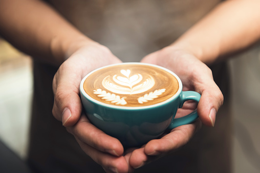 Barista hands holding a cup of coffee presenting beautiful Rosetta latte art pattern on surface