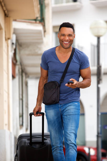 istock Handsome young man walking with suitcase and mobile phone 905883812