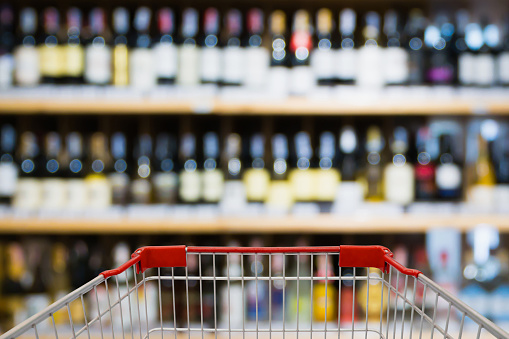 Shopping cart view with Abstract blur wine bottles on liquor alcohol shelves in supermarket or wine store background