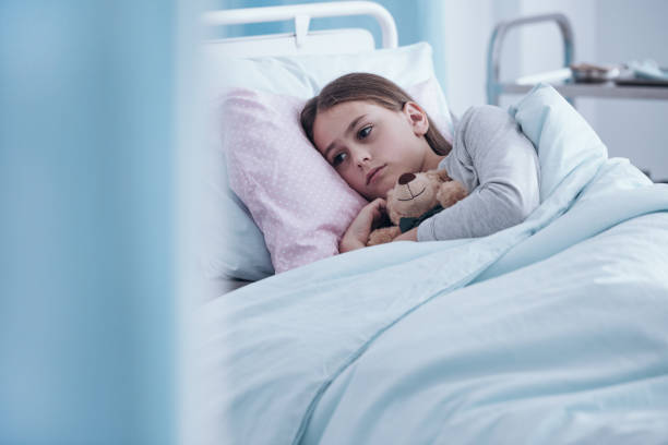 Sick girl in hospital bed In the background sick sad girl with teddy bear lying in hospital bed sick child hospital bed stock pictures, royalty-free photos & images