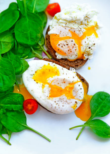 Tasty poached eggs on the bread with fresh green baby spinach and cherry tomatoes on the white plate, healthy dietary breakfast, delicious organic nutrition