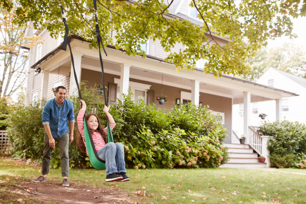 father pushing daughter on garden swing at home - swinging imagens e fotografias de stock