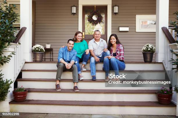 Parents With Adult Offspring Sitting On Steps In Front Of House Stock Photo - Download Image Now