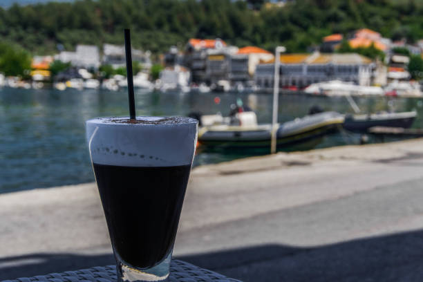 Iced freddo coffee with a straw on blurred background. Cold freddo cappuccino coffee with a black straw on a glass before blurred Greek island of Thassos background with copy space. freddo cappuccino stock pictures, royalty-free photos & images