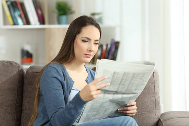 istock Serious woman reading a newspaper on a couch 905918462