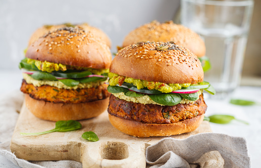 Camote al horno saludable hamburguesa con pan de grano entero, guacamole, mayonesa vegana y verduras sobre una plancha de madera. Concepto de comida vegetariana, fondo claro. photo
