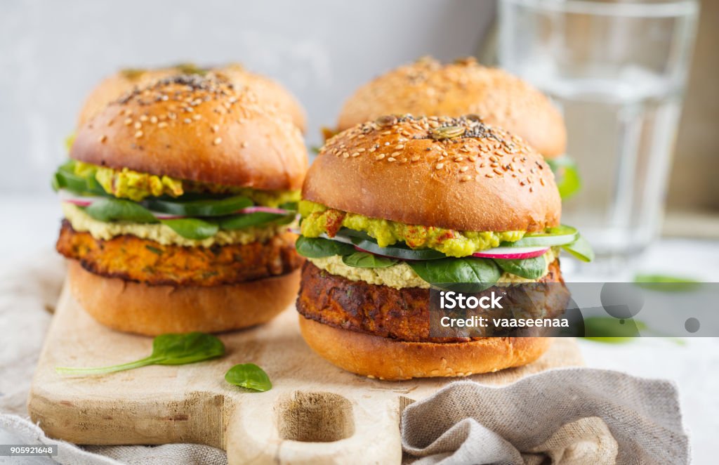 Camote al horno saludable hamburguesa con pan de grano entero, guacamole, mayonesa vegana y verduras sobre una plancha de madera. Concepto de comida vegetariana, fondo claro. - Foto de stock de Hamburguesa - Alimento libre de derechos