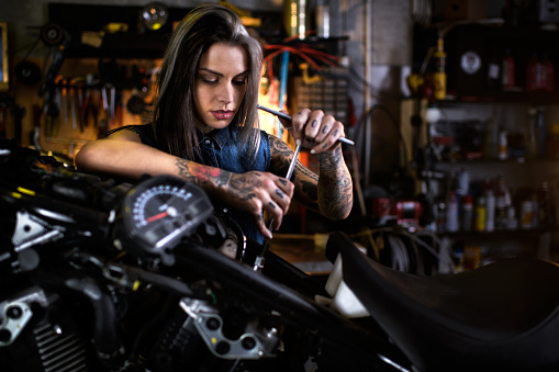 Tattoed female mechanic in auto repair shop is customizing motorcycle engine.
