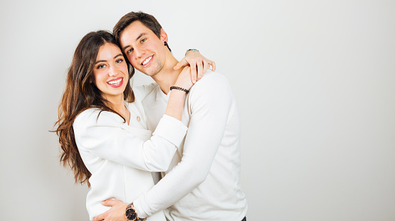 Portrait of a young and happy couple embracing wearing white clothes on white background