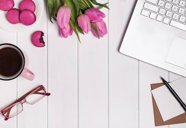 istock Woman's workplace with laptop, coffee pink tulips and macarons. 905923348