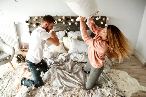 almohada y cariñosa pareja lucha en el dormitorio - bed couple pillow fight men fotografías e imágenes de stock