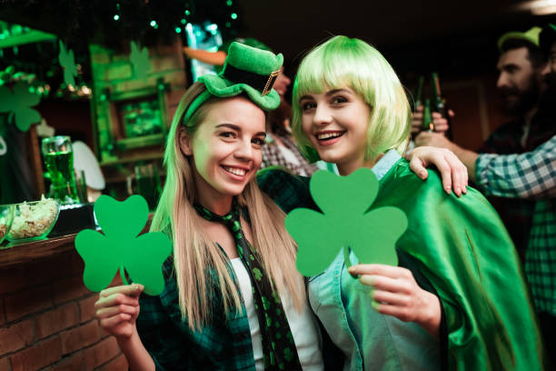 Two girls in a wig and a cap are photographed in a bar. Two girls in a wig and a cap are photographed in a bar. They celebrate St. Patrick's Day. They are having fun. One girl is holding a clover. st. patricks day photos stock pictures, royalty-free photos & images