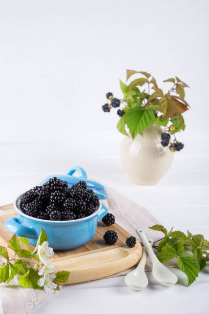 istock Ripe blackberries with leaves in a blue ceramic bowl on white table 905932924
