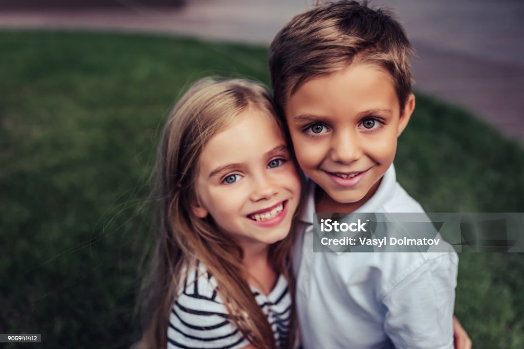 Children on green grass Couple of charming childs having fun outdoors. Portrait of beautiful girl and boy are hugging, smiling and looking at the camera. Little brother and sister in park on a green grass. Child Stock Photo