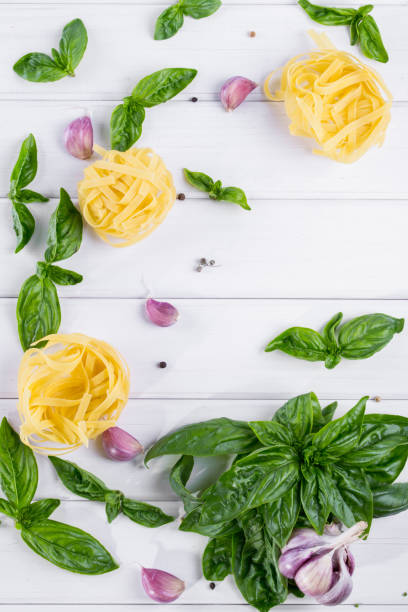 Fresh green basil with garlic  and raw pasta on white background. Flat lay.