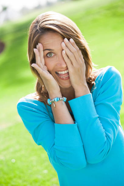 portrait of a smiling woman in summer who is hiding behind her hands
