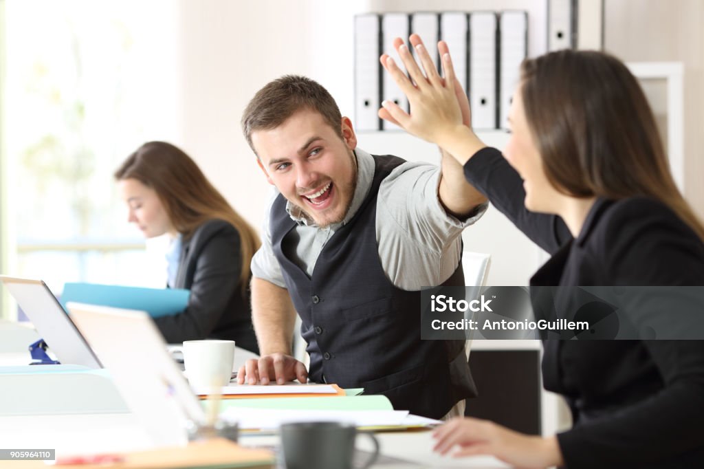 Coworkers celebrating achievement at office Two excited coworkers celebrating achievement giving five at office Reaching Stock Photo