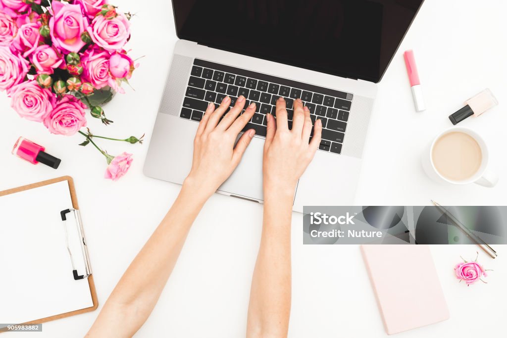 Jeune fille travaillant sur ordinateur portable. Bureau espace de travail avec des mains féminines, ordinateur portable, bouquet de roses roses, tasse à café, journal sur tableau blanc. Vue de dessus. Poser de plat. - Photo de Ordinateur libre de droits