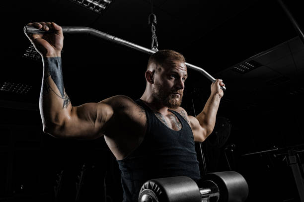 Professional athlete performs an exercise in the gym. Pulls the bar to the back of the head.