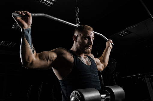 Professional athlete performs an exercise in the gym. Pulls the bar to the back of the head. Exercise for development of back muscles