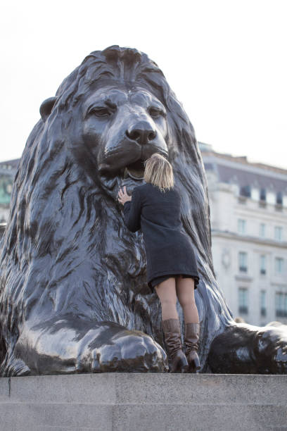 donna che bacia una delle famose statue di leoni a trafalgar square, londra - lion statue london england trafalgar square foto e immagini stock