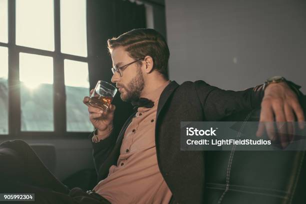 Stylish Young Businessman In Eyeglasses And Bow Tie Drinking Whiskey Stock Photo - Download Image Now