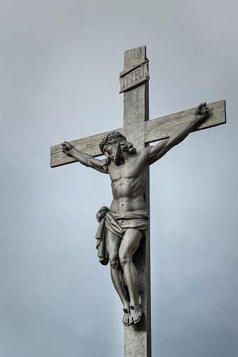 A wood carving of Jesus Christ on the Cross against an overcast gray sky
