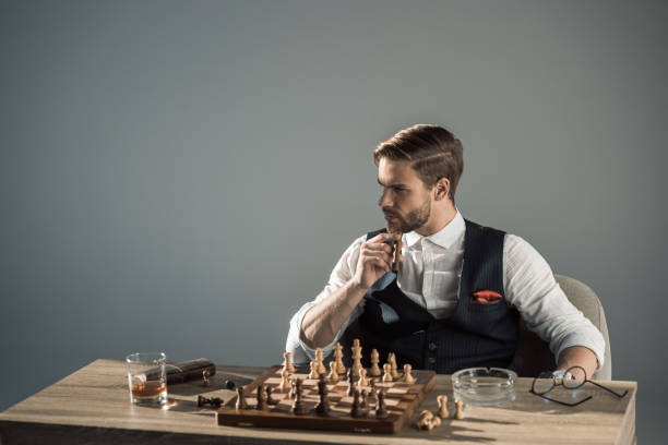 istock young man smoking cigar and looking away while playing chess 905996074