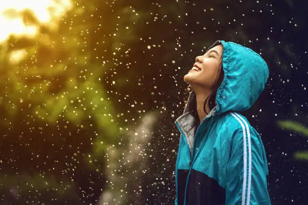 Photo of Asian woman wearing a raincoat outdoors. She is happy.