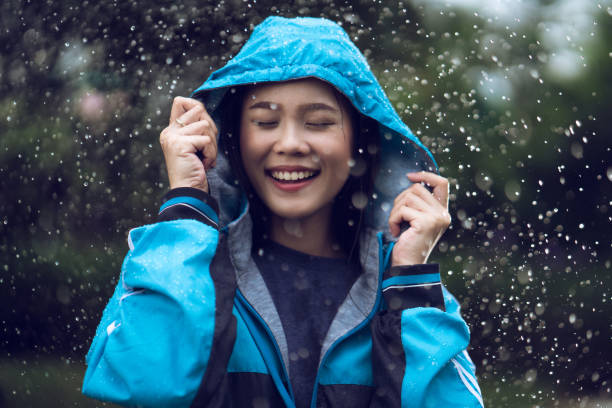 屋外でレインコートを着たアジア人女性。彼女は幸せです。 - umbrella women storm yellow ストックフォトと画像