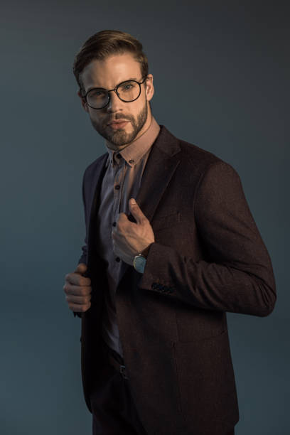 istock handsome stylish bearded man in wristwatch and spectacles looking at camera isolated on grey 905997526