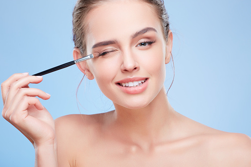 Beauty concept, head and shoulders of young woman with closed eye, smiling. Closeup of girl looking at camera and touching eyelid with brush, painting with eyeshadows.