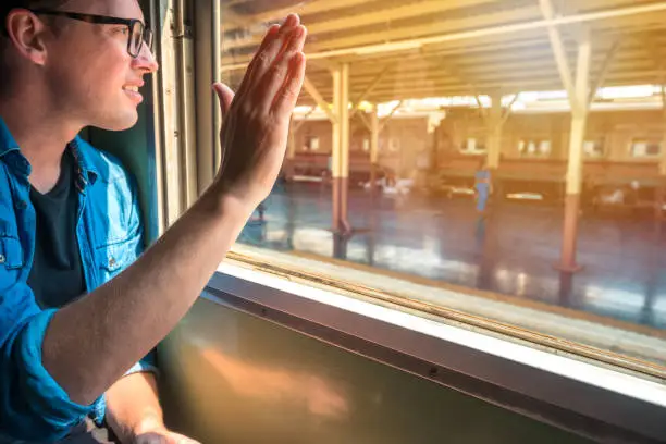 Man sitting in a train raise his hand to say hello or goodbye