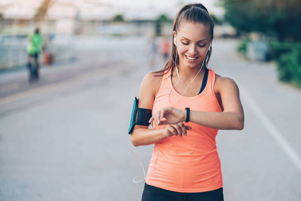 Wearable tech Smiling young sportswoman with arm band and headphones taking pulse stock pictures, royalty-free photos & images