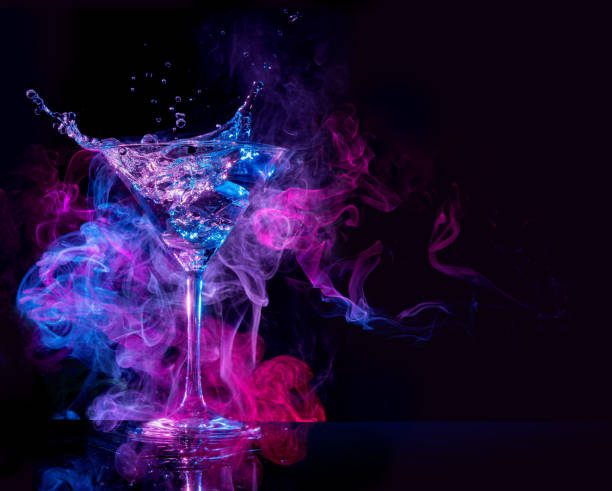 cocktail splashing in a smoky background cocktail splashing and multicolored smoke in a black background martini glass photos stock pictures, royalty-free photos & images