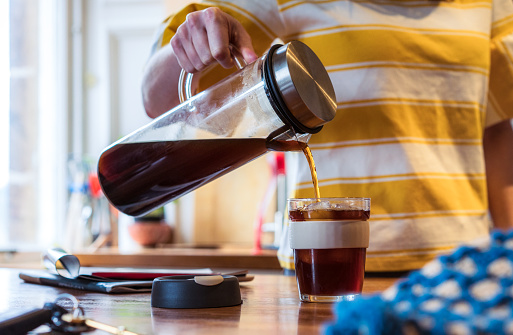 A woman pouring cold-brew coffee into a re-usable mug in the kitchen.