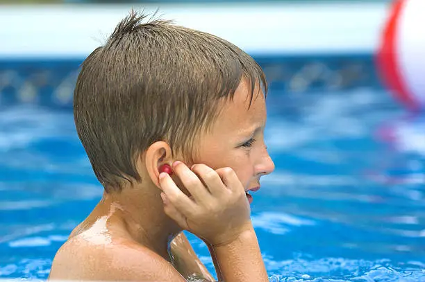 Young Boy Making sure his earplugs are in while playing in the pool