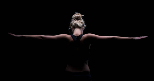 Beautiful fit and healthy blond woman in black top in the dark with arms stretched from behind stock photo