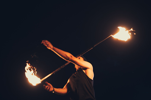 Young and strong man creating a performance with a contact staff, lit on fire.