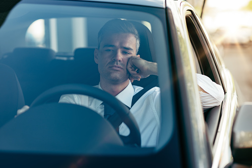 Pensive disappointed businessman sitting in his car and thinking with hand on chin