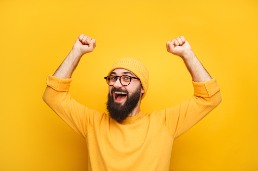 Cheerful bearded man in yellow clothes feeling happy and posing with hands up.