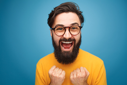 Excited handsome bearded man in glasses posing on blue background.