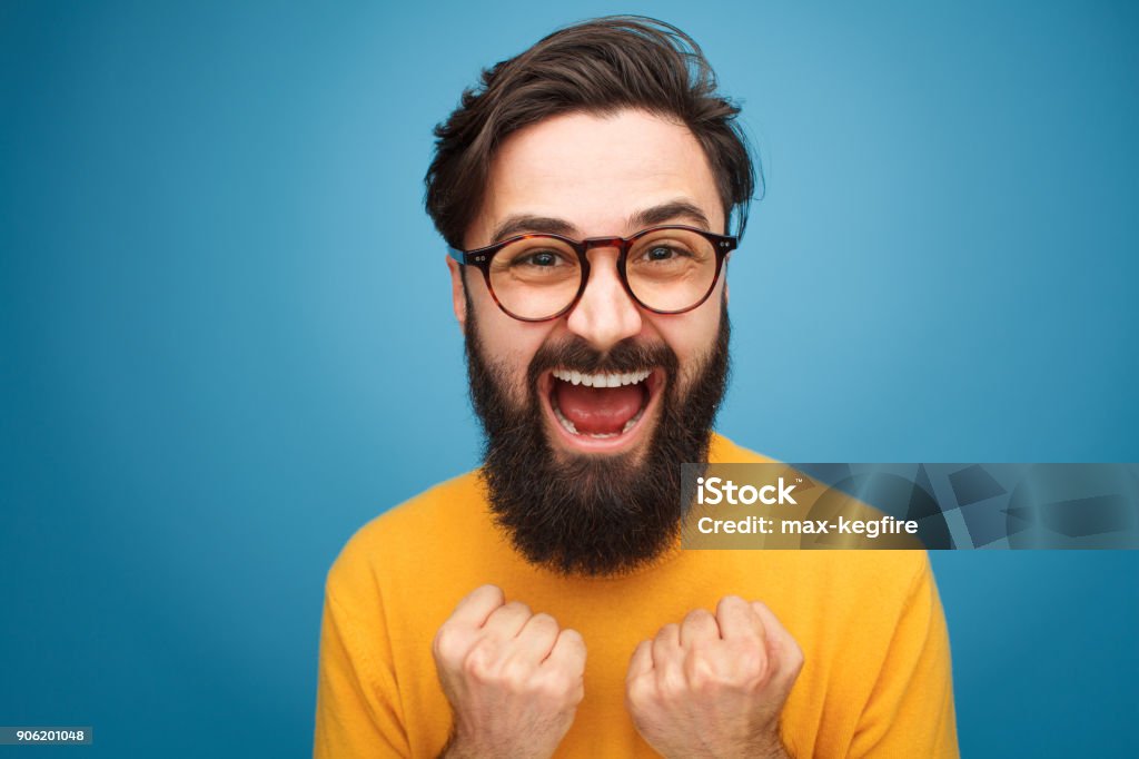 Excited bearded man in glasses Excited handsome bearded man in glasses posing on blue background. Men Stock Photo