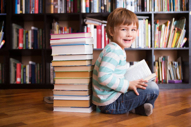 preschooler little boy reading a book in the library. the little boy with books near a bookcase stock photo