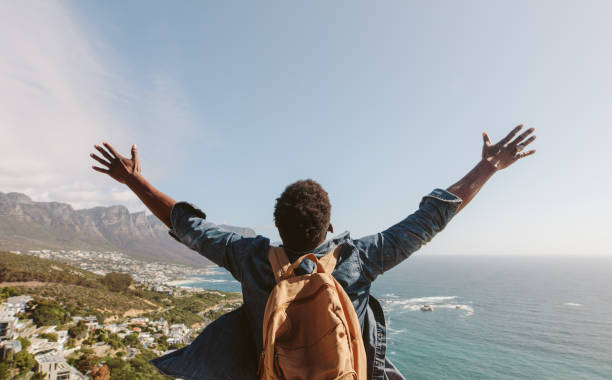 Man enjoying the view from top of mountain Rear view of young guy with backpack standing outdoors with arms spread open against seascape. Man enjoying the view from the top of the mountain. arms outstretched stock pictures, royalty-free photos & images