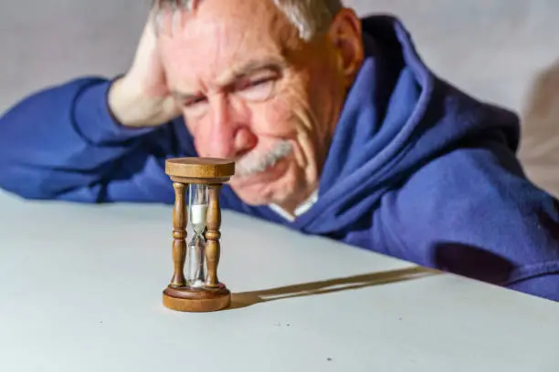 Senior man watching a time slip away as sand falls through an hourglass